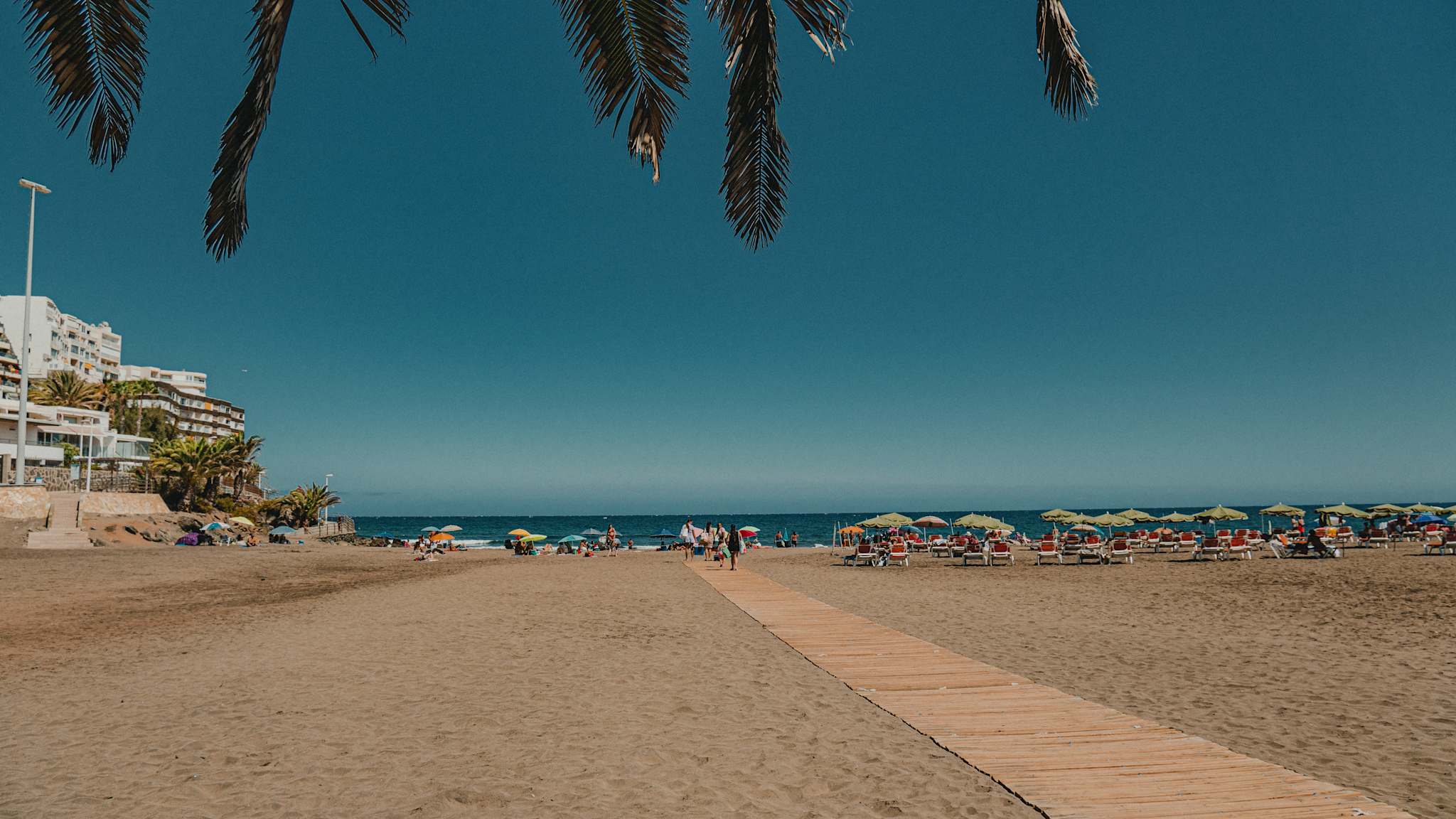 Ein langer Holzsteg an einem Strand mit Sonnenschirmen